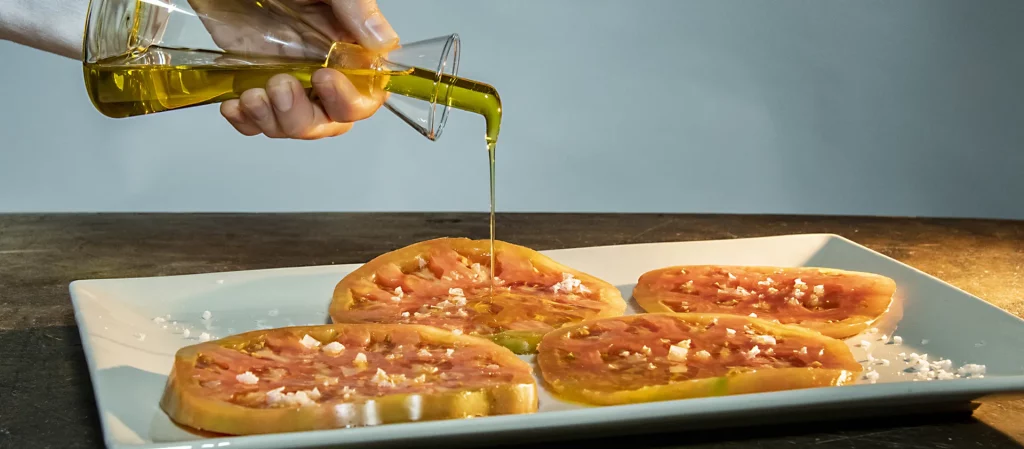 Cocinero vertiendo Aceite de Oliva Virgen Extra sobre rodajas de tomate rosa de Barbastro